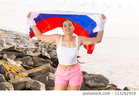 Young woman on coast posing with flag of Russia 113262959