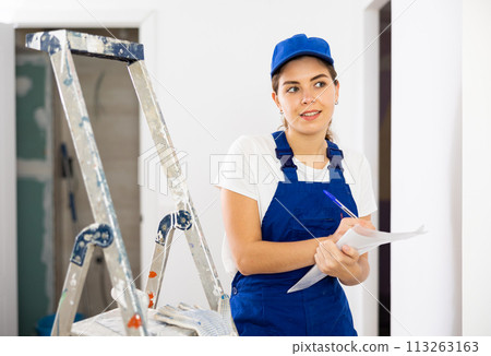 Woman in blue overalls checks the completed construction work on drawing Woman in blue overalls checks the completed construction work on drawing 113263163