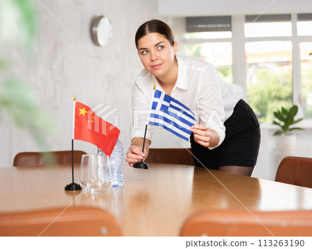Young female attendant putting up flags for international negotiations between china and greece Young female attendant putting up flags for international negotiations between china and greece 113263190