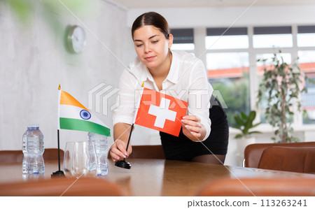 Employee of delegation prepares negotiating table - sets up flag of India and Switzerland 113263241