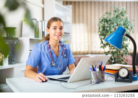 Smiling young woman therapist filling up medical forms on laptop in office Smiling young woman therapist filling up medical forms on laptop in office 113263288