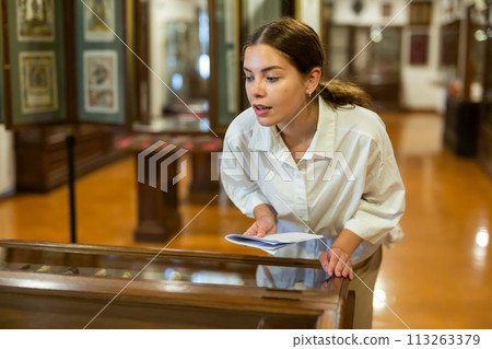 Woman looking at exhibits in glazed stands in museum Woman looking at exhibits in glazed stands in museum 113263379