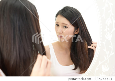 A woman looking in the mirror and worrying about damaged hair 113264524