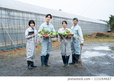 Farmers holding crops in front of a vinyl greenhouse 113264687