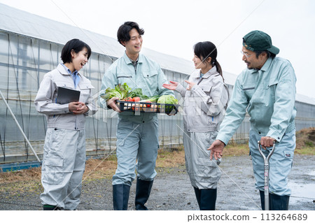 Farmers holding crops in front of a vinyl greenhouse 113264689