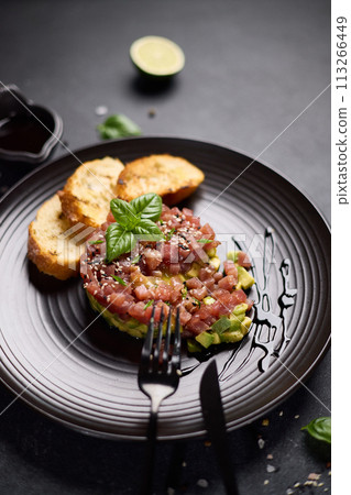 Tuna and avocado tartare with sesame seeds, capers and egg yolk on a dark ceramic plate with baguette bread crouton chips Tuna and avocado tartare with sesame seeds, capers and egg yolk on a dark ceramic plate with baguette bread crouton chips 113266449