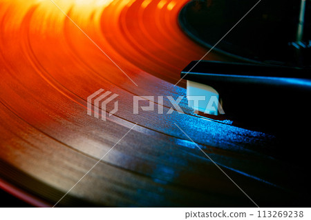 Close up photo of analog music player playing on turntable with needle illuminated in warm, cozy sunset light. Close up photo of analog music player playing on turntable with needle illuminated in warm, cozy sunset light. 113269238