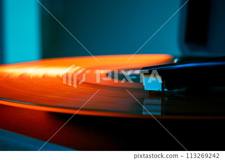 Detailed photo of phonograph needle riding waves of vinyl's surface in orange hues. Retro vinyl record player, bright lights. Detailed photo of phonograph needle riding waves of vinyl's surface in orange hues. Retro vinyl record player, bright lights. 113269242