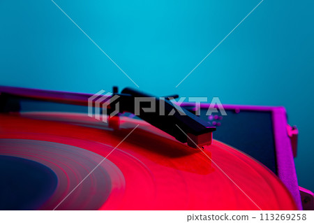 Vinyl record player, bright lights disco-bokeh. Needle on vinyl record in bright pink neon light against gradient blue background. Vinyl record player, bright lights disco-bokeh. Needle on vinyl record in bright pink neon light against gradient blue background. 113269258
