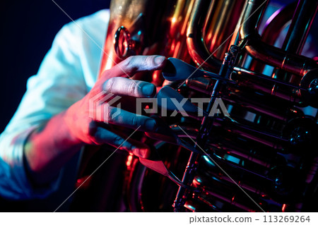 Close up photo with hands of trumpeter who plays chords on trumpet fingering in neon light of stage backlight. Close up photo with hands of trumpeter who plays chords on trumpet fingering in neon light of stage backlight. 113269264