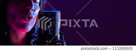 Banner. Close up of female vocalist singing passionately near studio microphone with purple flare lighting. Negative space to insert text. 113269305