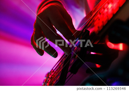 Close up photo of musician's hand on guitar neck with blue backlight and hazy smoke, highlighting musical performance. 113269346