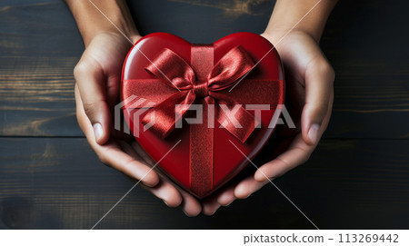 top view of closeup African American male hands holding gift heart shaped box with red bow 113269442
