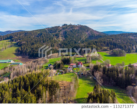 A serene landscape featuring the lush slopes of Tanvaldsky Spicak mountain during spring, with adjacent meadows and a cluster of buildings at the base. Tanvald, Czechia A serene landscape featuring the lush slopes of Tanvaldsky Spicak mountain during spring, with adjacent meadows and a cluster of buildings at the base. Tanvald, Czechia 113271377