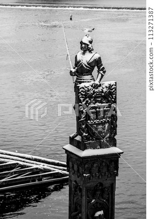 The statue of Bruncvik stands majestic in winter, towering above the Charles Bridge with a layer of snow adorning its head and shoulders. Prague, Czechia. Black and white photography. 113271387