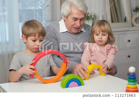 Grandfather playing toys with grandson and young granddaughter indoor. Old man grandpa studying with his grandchildren at weekend. Senior male having fun with kids. Happy multigeneration family vibe Grandfather playing toys with grandson and young granddaughter indoor. Old man grandpa studying with his grandchildren at weekend. Senior male having fun with kids. Happy multigeneration family vibe 113271663