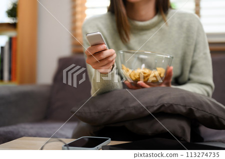 Cropped shot of young woman with remote control in hand watching TV in living room 113274735