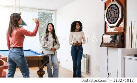 Happy diverse female friends playing dart in game room at home Happy diverse female friends playing dart in game room at home 113275012