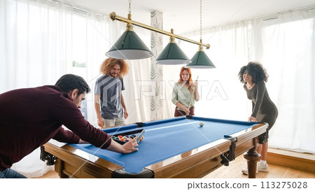 Man arranging balls for multiethnic friends playing pool in game room 113275028