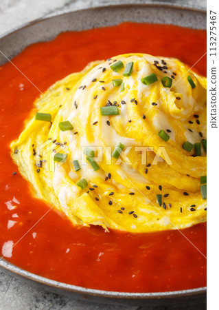 Tornado omelet a Korean dish called a tornado omurice, where a whirlwind of scrambled egg is placed over a mound of rice, and surroun sauce closeup on the plate. Vertical 113275467
