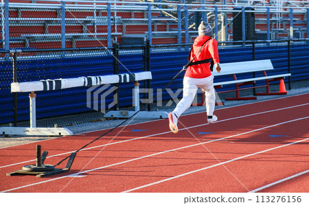 Male runner running while pulling a sled with weight on top on a track Male runner running while pulling a sled with weight on top on a track 113276156