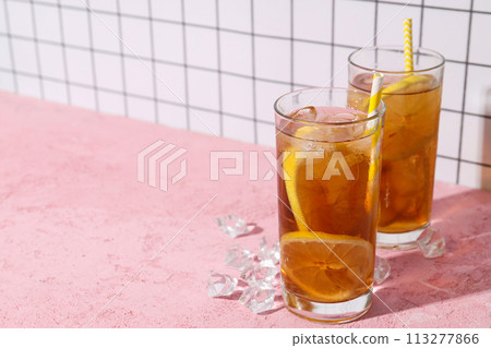 A glass of cold tea with ice and an orange on a pink background A glass of cold tea with ice and an orange on a pink background 113277866