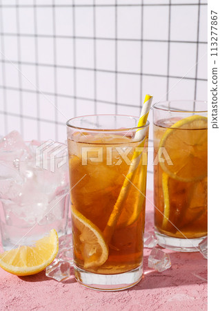 A glass of cold tea with ice and an orange on a pink background A glass of cold tea with ice and an orange on a pink background 113277867