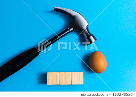 Hammer is hitting on an egg with blue background. minimal idea creative concept. Hammer is hitting on an egg with blue background. minimal idea creative concept. 113278526