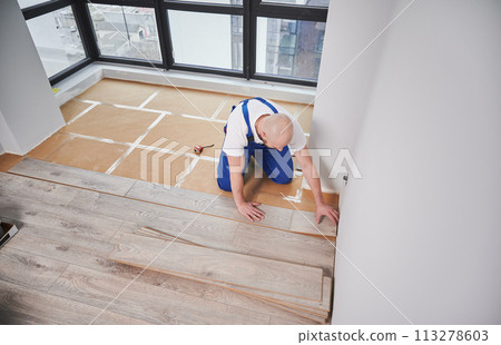 Top view of man construction worker laying laminate wood plank on floor underlayment in living room. Man installing laminate timber flooring in apartment under renovation. 113278603