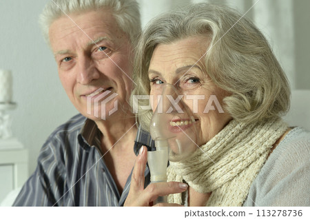 An elderly couple is sick and uses an inhaler 113278736