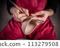 A woman is making a pottery bowl with a brush and a tool 113279508