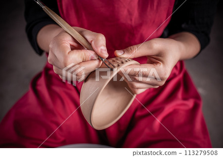 A woman is making a pottery bowl with a brush and a tool A woman is making a pottery bowl with a brush and a tool 113279508