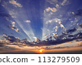 The sky is blue with a few clouds and the sun is setting 113279509