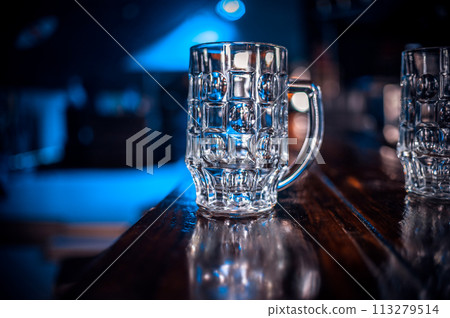 A glass mug is sitting on a wooden bar counter A glass mug is sitting on a wooden bar counter 113279514