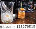 A glass of liquor with a garnish on top sits on a wooden table 113279515