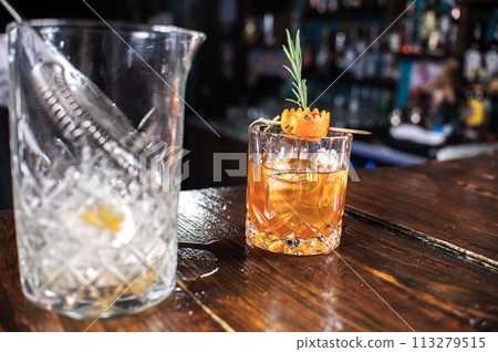 A glass of liquor with a garnish on top sits on a wooden table 113279515
