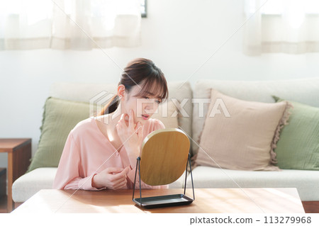 Middle-aged woman looking in the mirror and checking her skin (Beauty/Skincare) 113279968