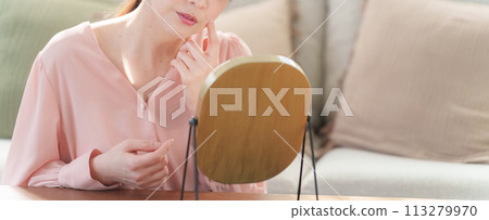 Middle-aged woman looking in the mirror and checking her skin (Beauty/Skincare) 113279970