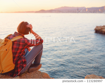 Young woman hiking on rocky beach in Spain, Benidorm. Watching the choppy sea and the bay. traveler enjoying freedom in serene nature landscape 113280997