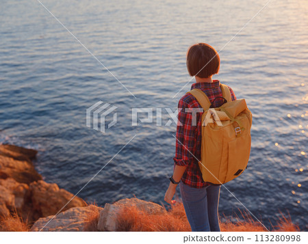 Young woman hiking on rocky beach in Spain, Benidorm. Watching the choppy sea and the bay. traveler enjoying freedom in serene nature landscape 113280998