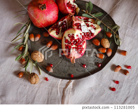 Image of Still Life with Turkish Pomegranate and olive branch on old retro plate. Dark wood background, antique copper plate. Fresh ripe whole pomegranates, opened pomegranate and seeds 113281005
