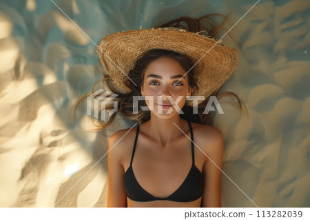 A beautiful girl lies in a black swimsuit on golden sand on a bright sunny day. Go-pro shot. top view, girl in a hat. distant perspective. The girl smiles. A beautiful girl lies in a black swimsuit on golden sand on a bright sunny day. Go-pro shot. top view, girl in a hat. distant perspective. The girl smiles. 113282039