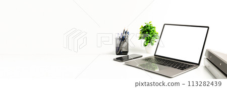 Blank white screen laptop on a white table in the office. Working concept using technology smartphones, notebook, internet. Copy space on left for design or text, Closeup, Gray, and blurred background 113282439
