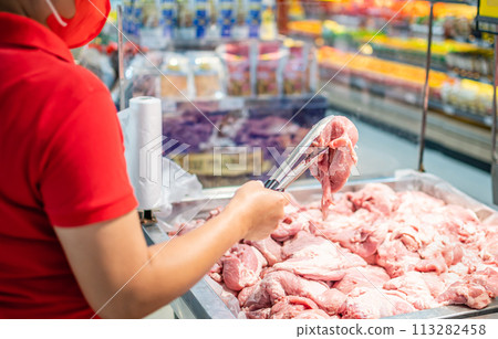 A woman holds and looks at fresh pork to buy quality pieces at the fresh produce section of the supermarket. Close up, Selective focus, Blurred background, Copy space for text or design. 113282458