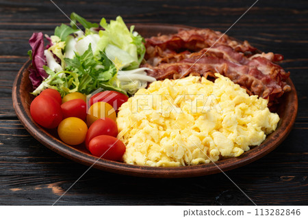 Breakfast plate . Scrambled eggs , bacon , cherry tomatoes and salad 113282846