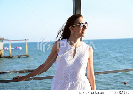 a girl in a summer white dress on the seashore enjoys life and looks into the distance a girl in a summer white dress on the seashore enjoys life and looks into the distance 113282932