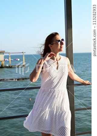 a girl in a summer white dress on the seashore enjoys life and looks into the distance a girl in a summer white dress on the seashore enjoys life and looks into the distance 113282933