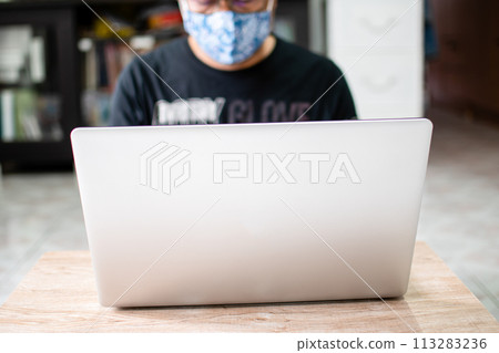 The masked man was working at home using a laptop, communicating via the internet with a customer during the coronavirus or COVID-19 outbreak, and as a preventive measure. copy space on left put text 113283236
