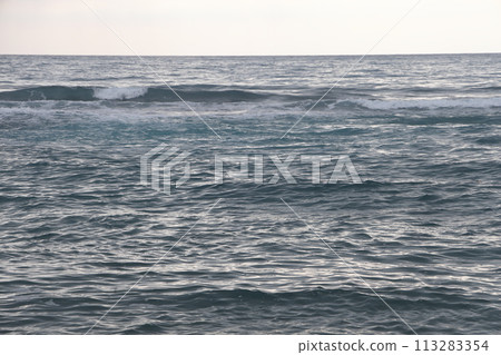 A lone figure in front of foam waves and a historic mountain in Alanya, November 2021. 113283354