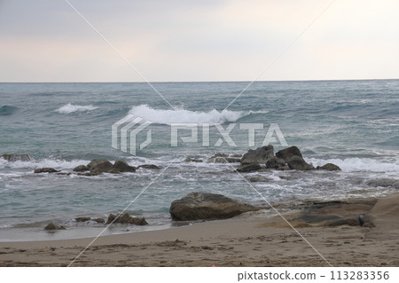 A lone figure in front of foam waves and a historic mountain in Alanya, November 2021. 113283356